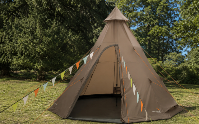 Brown teepee-style tent with open entrance, colorful pennant bunting in front, grass and trees in the background