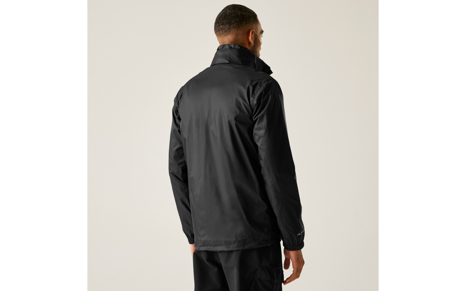 Person von hinten, trägt schwarze Jacke und schwarze Hose, heller einfarbiger Hintergrund