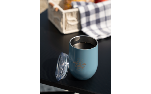 Blauwe thermosbeker met deksel op zwarte tafel, witte krat en blauw-wit geruit doek op de achtergrond