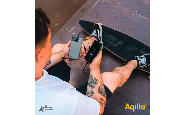 Un homme avec des tatouages tenant deux smartphones dans ses mains, assis sur un sol en carreaux rouges