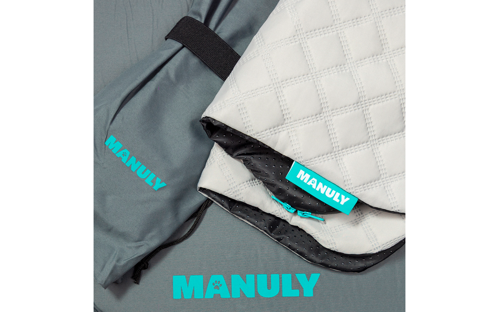 Gestepptes weiß-graues Textil mit Rautenmuster, schwarzer Innenseite mit Punkten und türkisem 'MANULY'-Etikett; daneben graue Tasche mit elastischem Riemen und türkisem 'MANULY'-Schriftzug