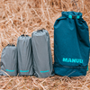 Drei graue, gepackte Packbeutel und eine größere türkisblaue Rolltop-Tasche mit der Aufschrift "MANULY" auf trockenem Gras