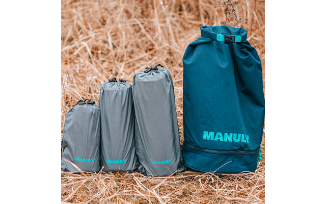 Drei graue, gepackte Packbeutel und eine größere türkisblaue Rolltop-Tasche mit der Aufschrift "MANULY" auf trockenem Gras