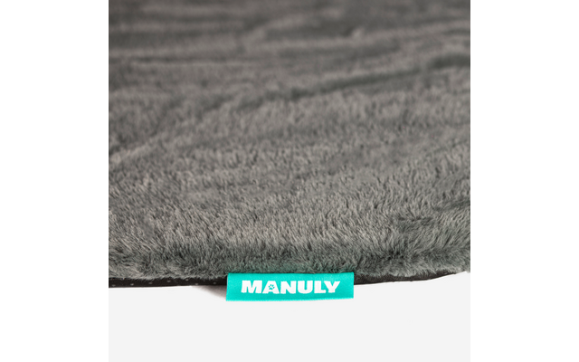 Grauer, flauschiger Teppichrand mit türkisem Textilschild „MANULY“ auf weißem Hintergrund