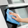 Hand mit blauem Tuch an der Griffstange und Glastür eines Backofens