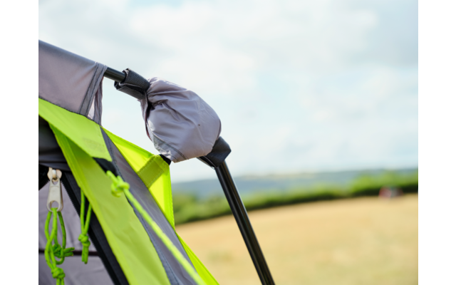 Nahaufnahme eines grauen und neongrünen Zelts mit schwarzem Gestängebogen und grauer Abdeckung; im Hintergrund Feld und bewölkter Himmel