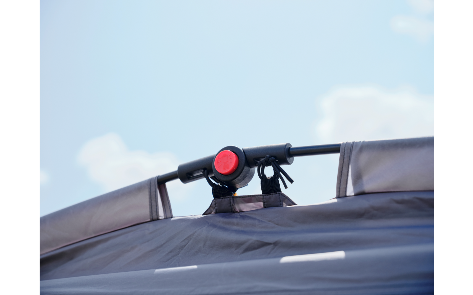 Schwarzer Griff mit rundem roten Knopf über grauem Verdeck vor blauem Himmel