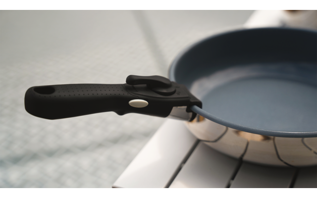 Eine schwarze Bratpfanne mit Holzgriff liegt auf einem weißen Untergrund
