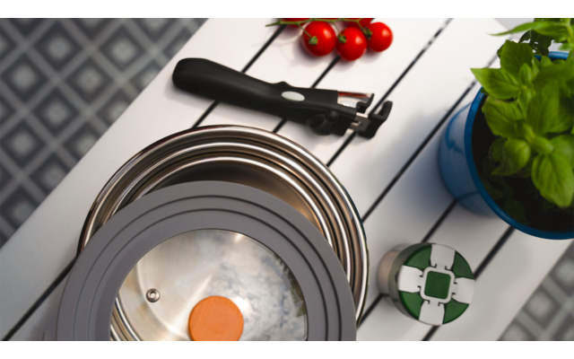 Kochfeld mit einem Ei in einer Pfanne, rote Kirschtomaten und eine grüne Pflanze daneben