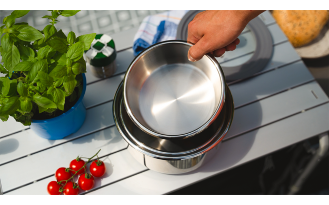 Hand gießt Wasser aus einem Kessel in eine Tasse auf einer Holzterrasse