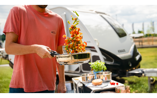 Person in orangehemden hält eine Gabel mit Gemüse über einem Grill im Freien