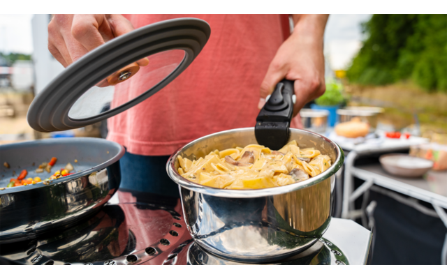 Person gießt gekochte Nudeln in einen Sieb über einem Topf in einer Küche im Freien