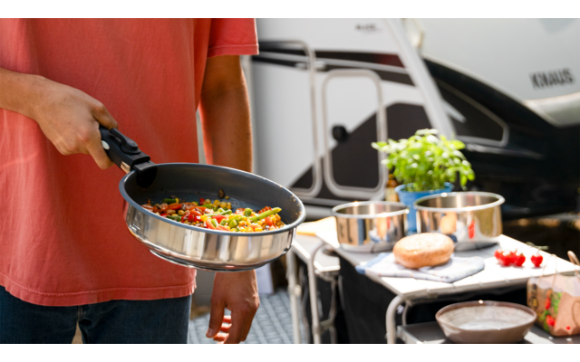 Person hält Teller mit angebratenem Gemüse vor Grill im Freien