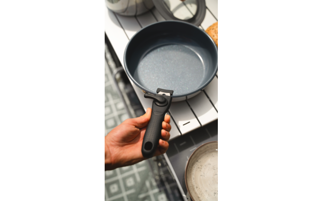 Hand hält schwarzen Topf mit Griff über Herd