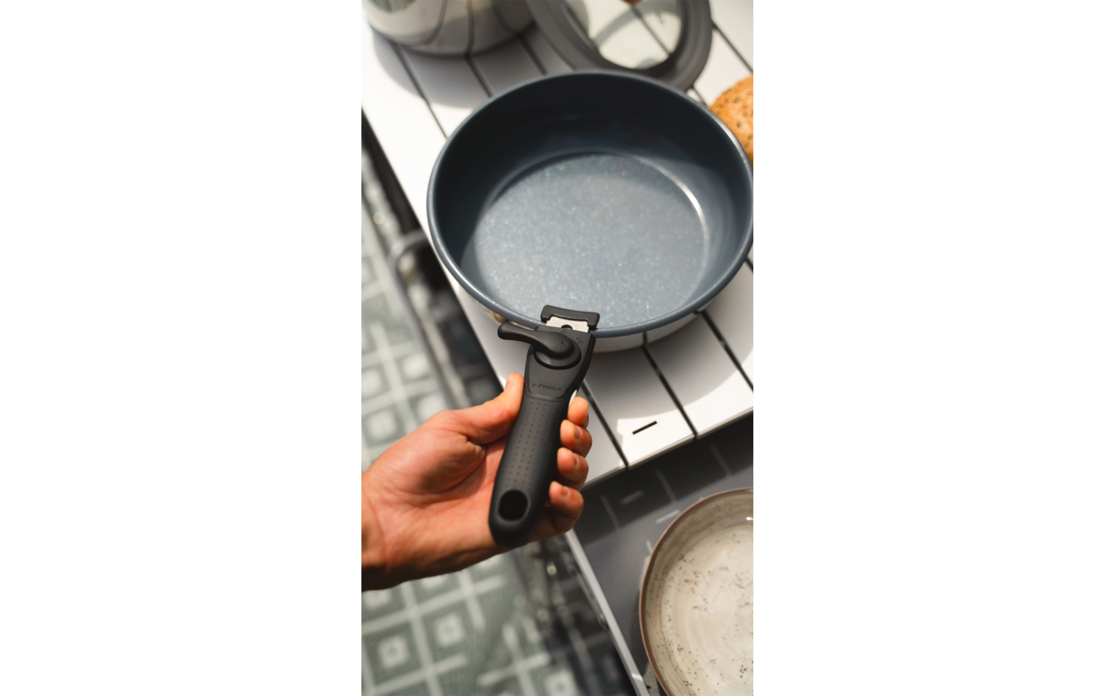 Hand hält schwarzen Topf mit Griff über Herd