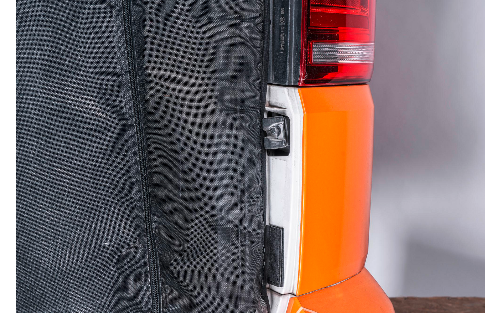Nahaufnahme eines Rücklichts an einem orangefarbenen Fahrzeug, rechts neben einem schwarzen Stoffdach