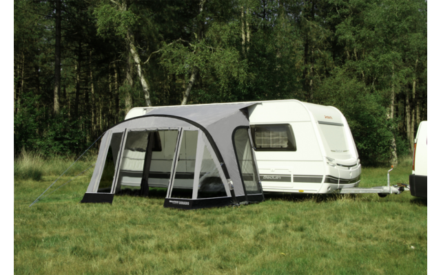 Caravan with attached awning on a grassy area in front of trees