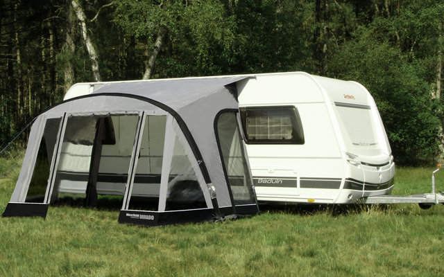 Wohnwagen mit angebautem Vorzelt auf einer Wiese vor Bäumen