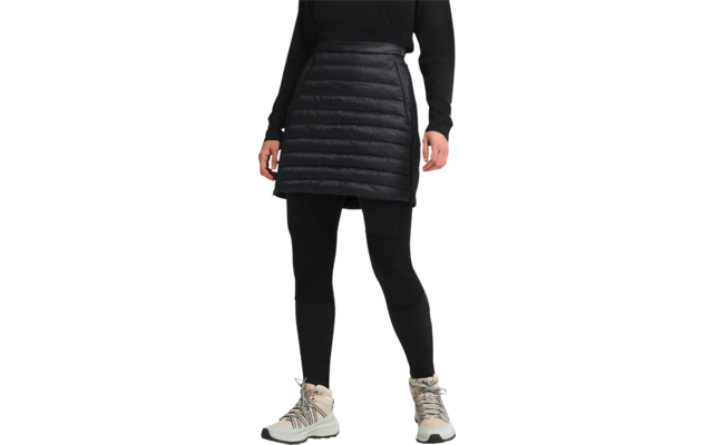 Frau trägt schwarzen Stepprock, schwarzen Pullover und weiße Sneaker