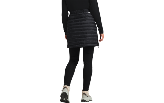 Person von hinten mit schwarzer gesteppter Jacke, schwarzem Rock und weißen Turnschuhen
