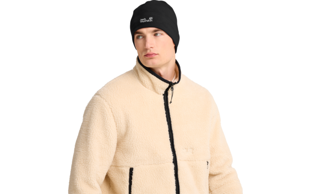 Mann, Brustbild, trägt beige Fleecejacke mit schwarzem Reißverschluss und schwarzen Taschenkanten, schwarzer Beanie mit weißem Logo, blickt nach links, weißer Hintergrund