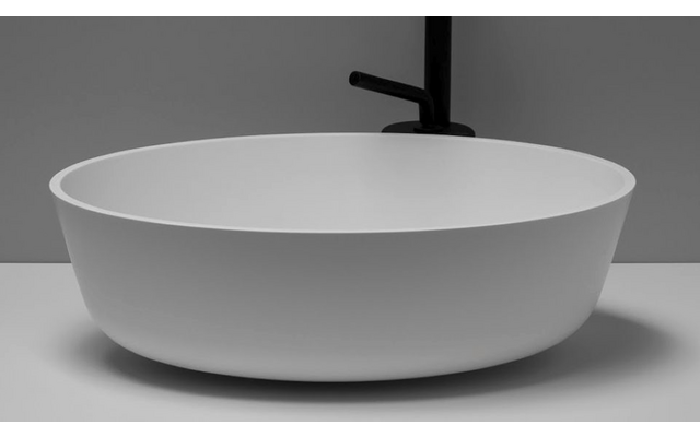 Ronde witte opzetwastafel op een licht werkblad, hoge matzwarte kraan erachter, grijze muur