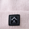 Gorro de punto rosa claro con vuelta y etiqueta cuadrada negra con un logo de montaña blanco y el texto DARE 2B