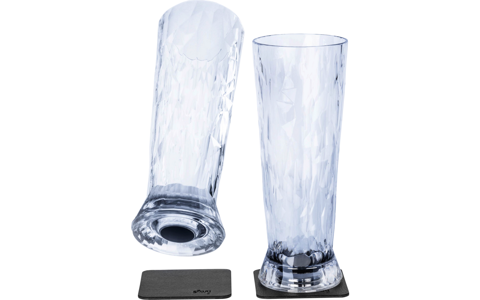 Deux grands verres transparents à motif facetté ; l'un est debout sur un dessous-de-verre carré et sombre, l'autre est couché sur le côté sur un deuxième dessous-de-verre