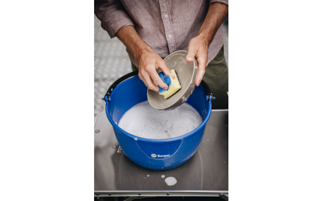 Handen scheppen water met een beker uit een blauwe emmer