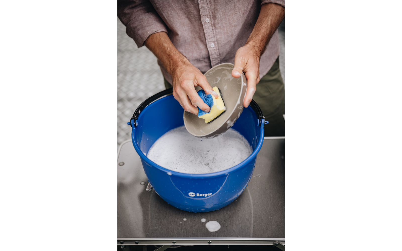 Handen scheppen water met een beker uit een blauwe emmer