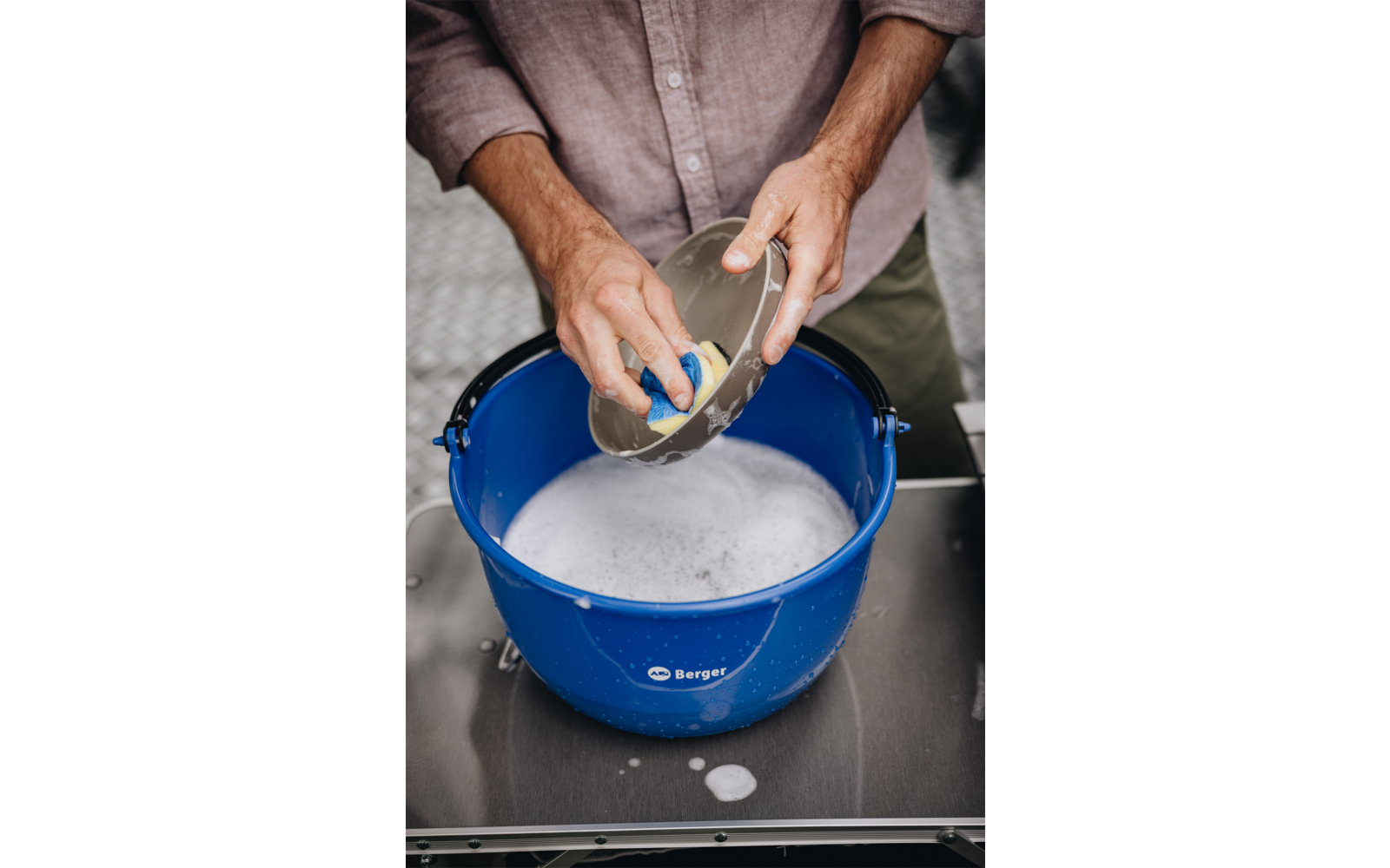 Handen wassen een bord boven een blauwe plastic kom met zeepsop