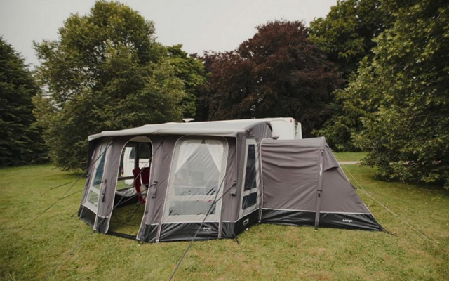 Una tenda da campeggio grigia e bianca su un prato con alberi sullo sfondo