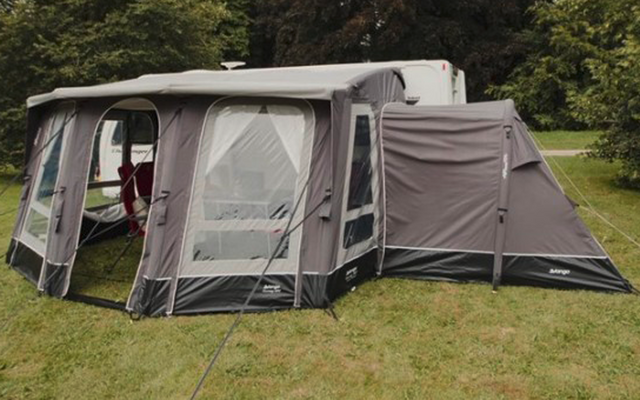 Een grijze en witte campertent op een grasveld met bomen op de achtergrond