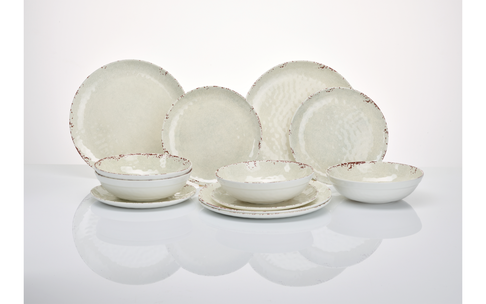 Mehrere cremefarbene Keramikteller und -schalen mit unregelmäßig braunem Rand auf weißer Fläche