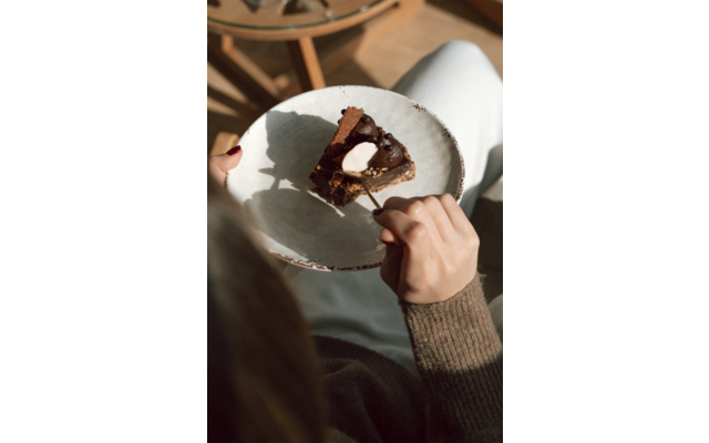 Stück Schokoladenkuchen mit Sahne auf einem runden Teller; eine Hand hält eine Gabel über dem Kuchen