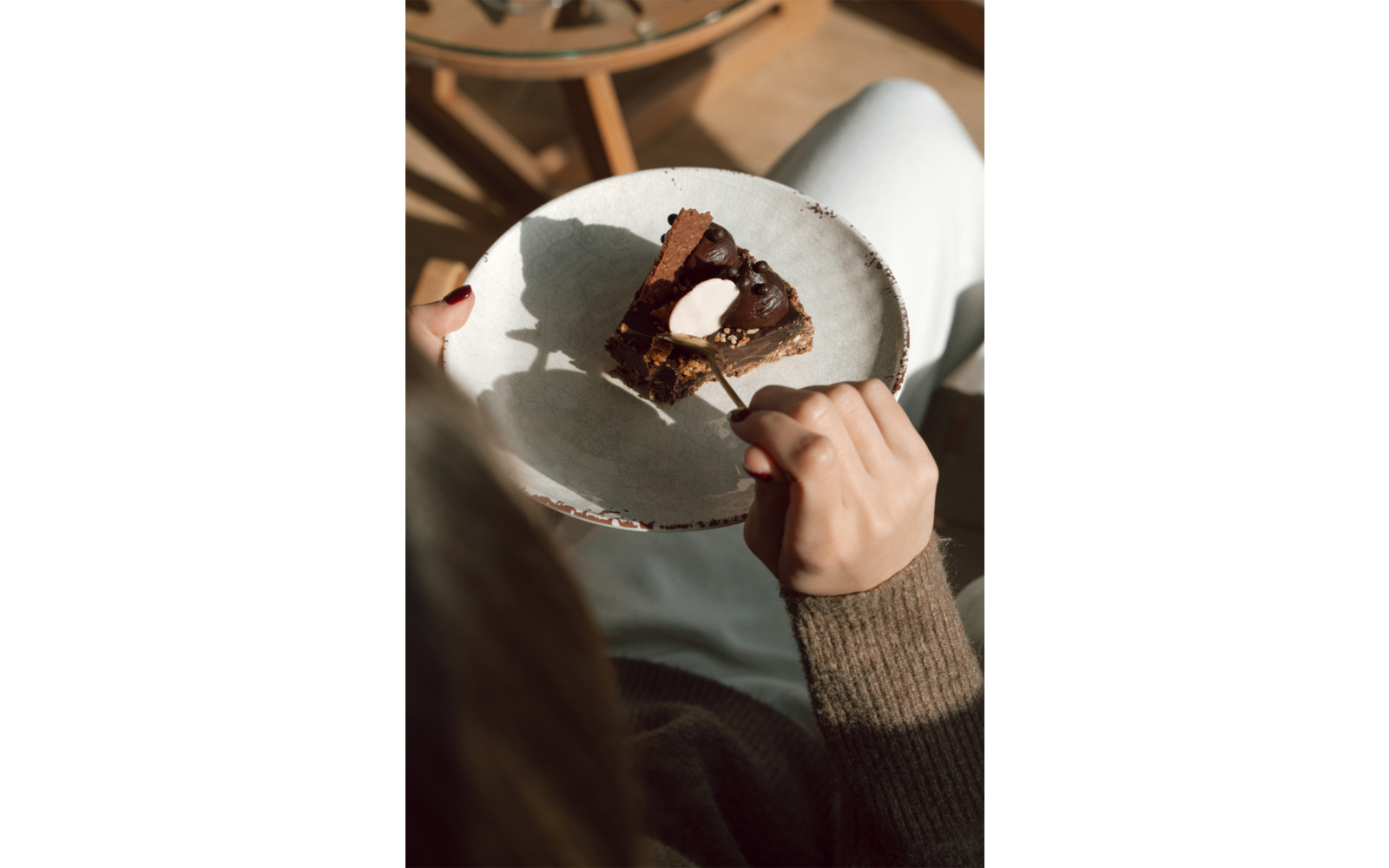 Stück Schokoladenkuchen mit Sahne auf einem runden Teller; eine Hand hält eine Gabel über dem Kuchen