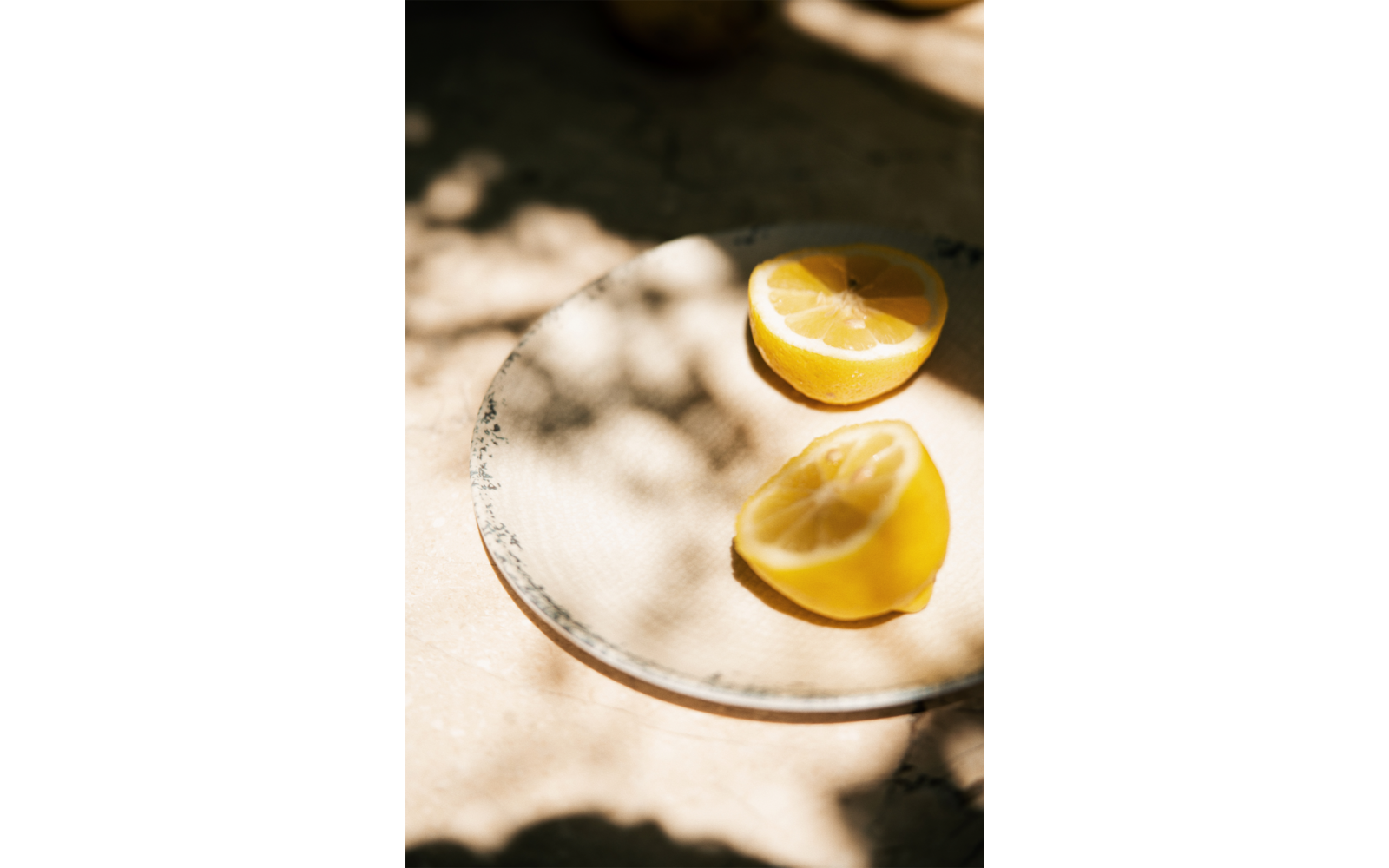 Zwei halbierte Zitronen auf einem runden Teller, Sonnenlicht und Schatten