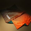 Spread-out orange sleeping bag with black dots, green inner lining and white brand text "TAMBU" on a beige background