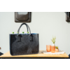 Graue Filztasche mit zwei Henkeln auf einer Holzfläche, aus der grüne Flaschenverschlüsse ragen; daneben zwei orangefarbene Gläser und zwei kleine Topfpflanzen auf einem weißen Tuch; heller Hintergrund mit zwei kleinen Fenstern