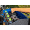 Blaue Tasche mit vier Plastikflaschen mit grünen Verschlüssen, drei Bechern mit Deckel und einer Hand, die einen Becher herausnimmt; Auto und Gras im Hintergrund