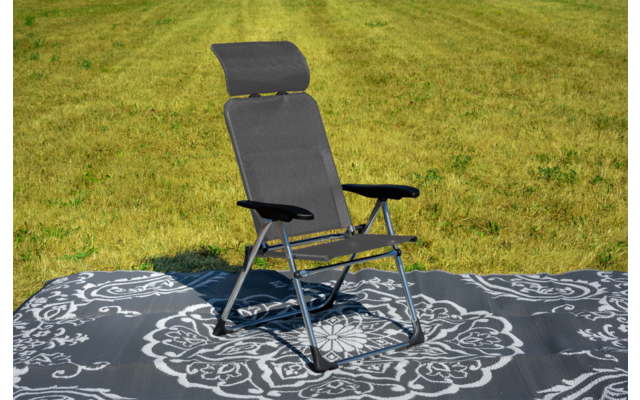 Schwarzer Klapp-Liegestuhl mit Kopfstütze und Armlehnen auf grauem, weiß gemustertem Outdoor-Teppich auf Gras