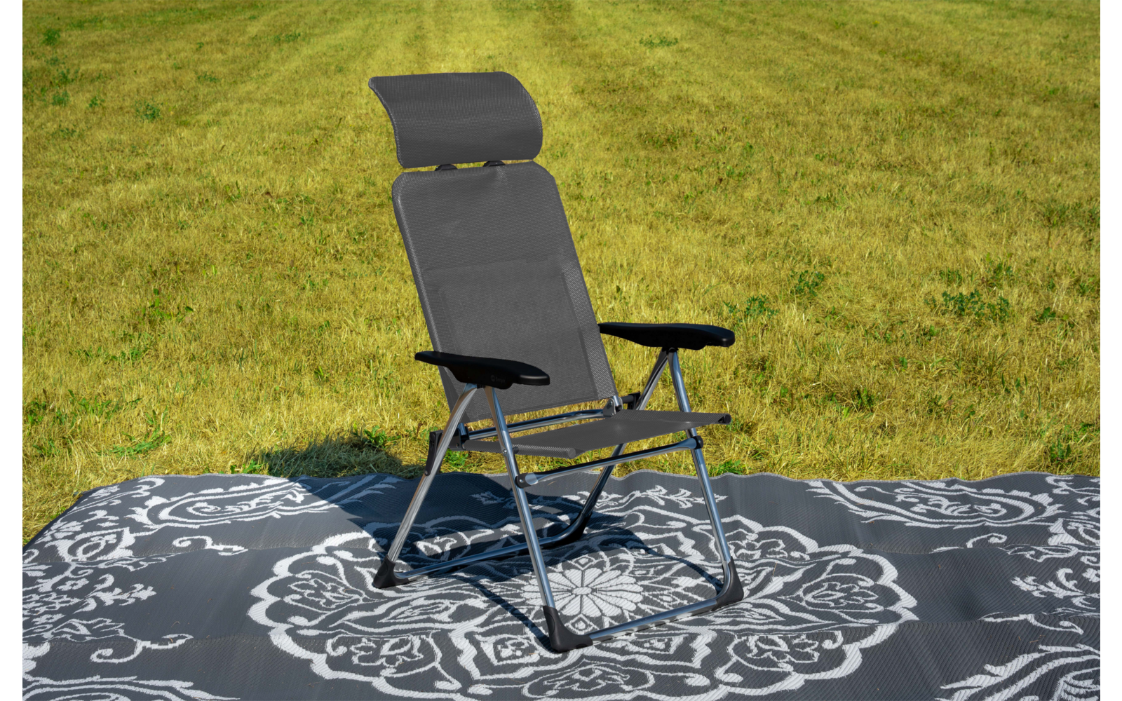 Schwarzer Klapp-Liegestuhl mit Kopfstütze und Armlehnen auf grauem, weiß gemustertem Outdoor-Teppich auf Gras