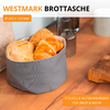 Sac à pain en tissu gris avec petits pains et croissant sur une table en bois; salière et poivrière, tasse blanche et planche en bois en arrière‑plan; texte 'WESTMARK BROTTASCHE', indication 'Ø 200 x 120 MM' et étiquette orange 'STILVOLLE AUFBEWAHRUNG FÜR BROT & MEHR'