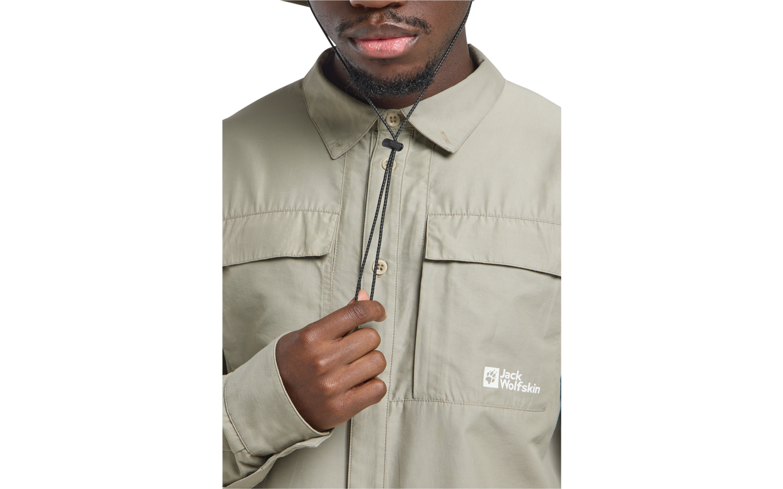 Oberkörper einer Person mit beigefarbener Jacke, unterer Gesichtsbereich (Mund, Kinn) sichtbar, Hand zieht Kordel am Kragen, Jack Wolfskin-Logo auf der Brust