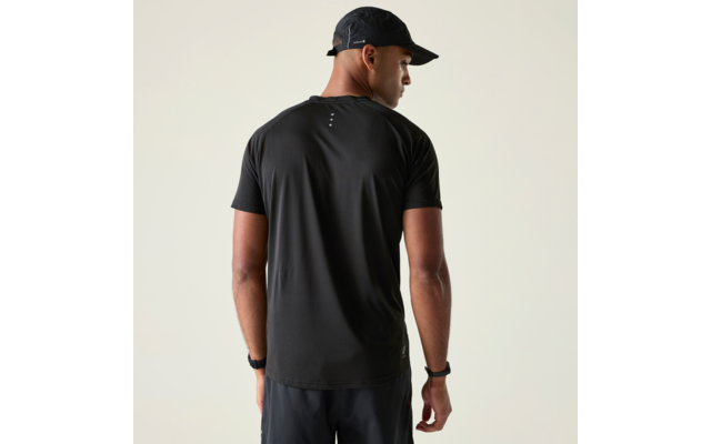 Person von hinten, trägt schwarzes kurzärmliges T‑Shirt, schwarze Kappe und schwarze Shorts, links eine Armbanduhr, vor hellem einfarbigem Hintergrund