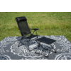 Fauteuil pliant noir en mesh avec appuie-tête et accoudoirs à côté d'un tabouret pliant assorti sur une couverture grise à motif blanc sur l'herbe