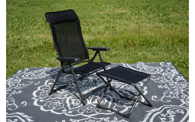 Chaise pliante noire avec accoudoirs et repose-pieds pliant noir sur une grande couverture gris et blanc à motif sur de l'herbe