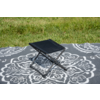 Petit tabouret pliant noir sur une couverture grise à motif blanc sur de l'herbe