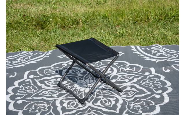 Petit tabouret pliant noir sur une couverture grise à motif blanc sur de l'herbe