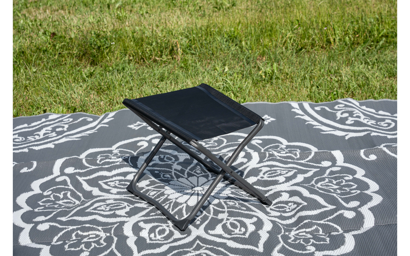 Petit tabouret pliant noir sur une couverture grise à motif blanc sur de l'herbe